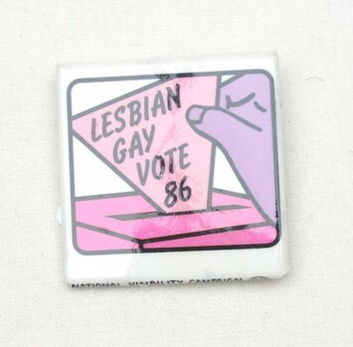 Square badge with a purple hand holding a pink triangle with the text: &quot;LESBIAN GAY VOTE 86&quot;. USA, 1986.