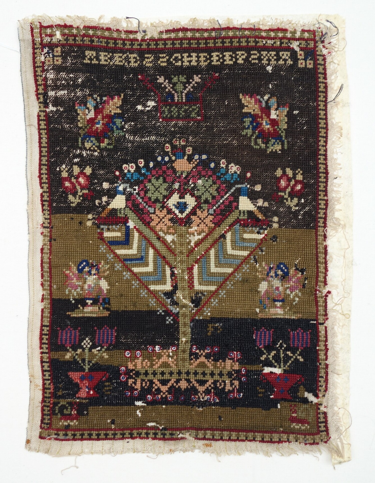 Sampler with a central stylised tree surrounded by floral motifs, all worked on a black ground (some of the black has faded to a brown colour). There is a date of 1852 and the name "AKKES S SCHEEEPSMA. (TRC 2021.1805)
