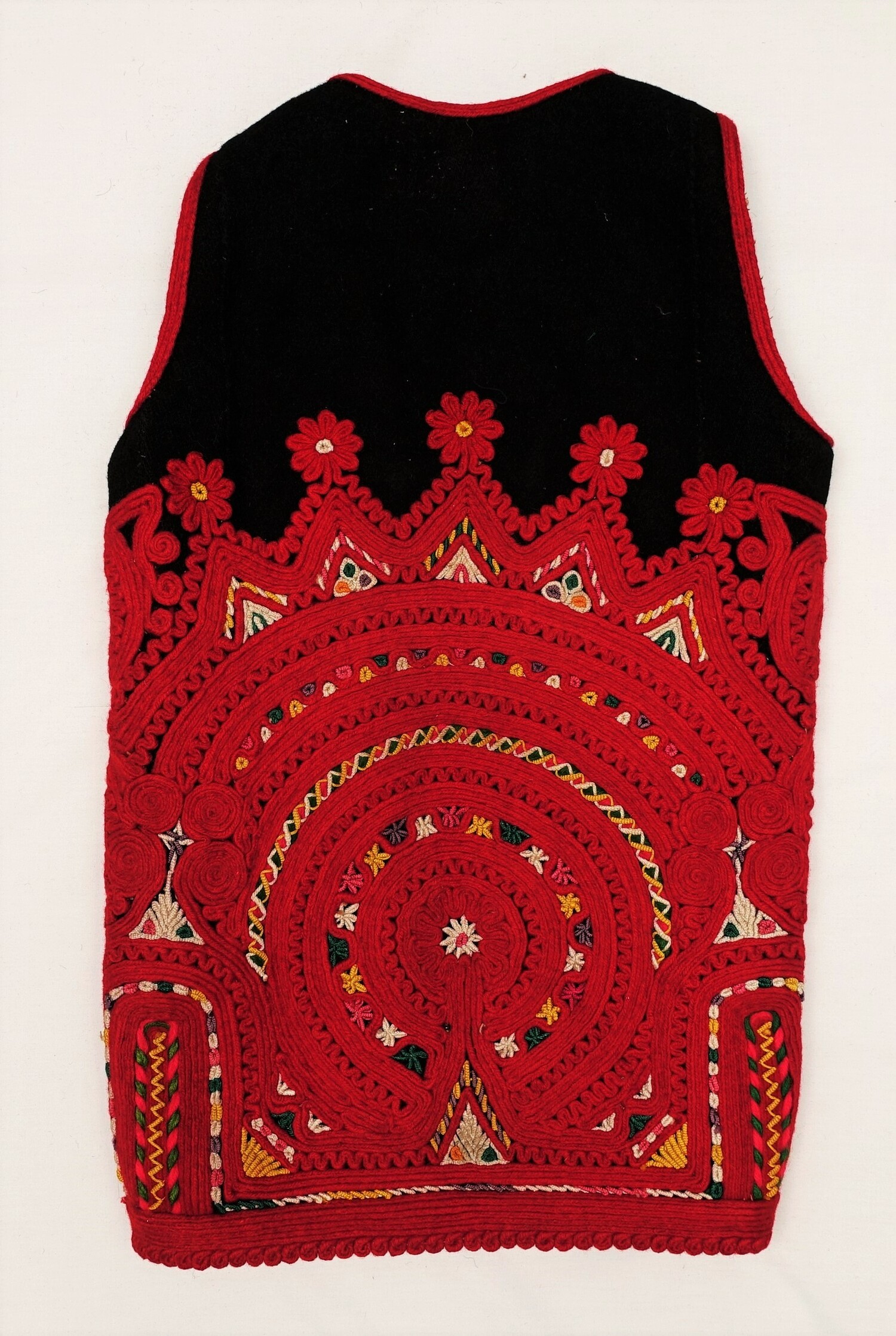 Embroidered back of a woman's waistcoat, Albania, 20th century (TRC 2022.0943a). The embroidery constitutes an intricate design of applied cords and braids in red wool, with details in bullion knots using white, yellow, purple and green cotton cord.
