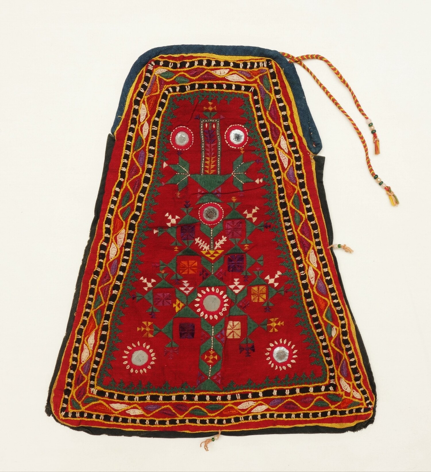Red, triangular bag decorated on both sides with geometric shapes including diamonds, triangles, chevrons and zig-zags, flanked by a line of rectangles in interlacing stitches alternating with glass mirrors in red frames. India, Rajasthan/Jodhpur, 1980 (TRC 2022.2110).