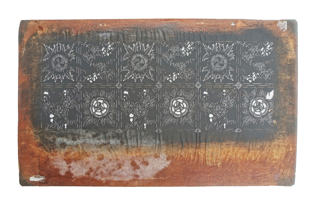 Paper stencil with two rows of a square trellis work pattern enclosing stylised floral motifs. Japan, mid-20th century (TRC 2023.0210).