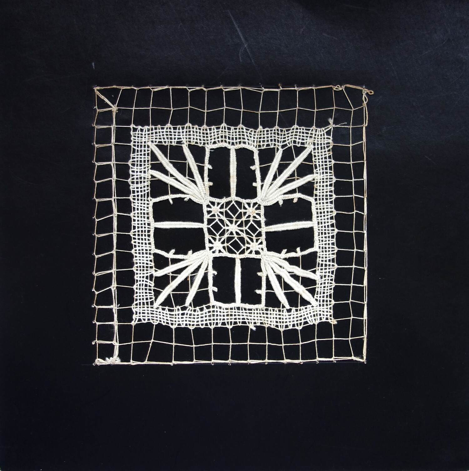 Piece of black card with a sample of square network with darned and needle woven patterns. Worked by G.H.P. Wening, c. 1922 (TRC 2023.2805.022).