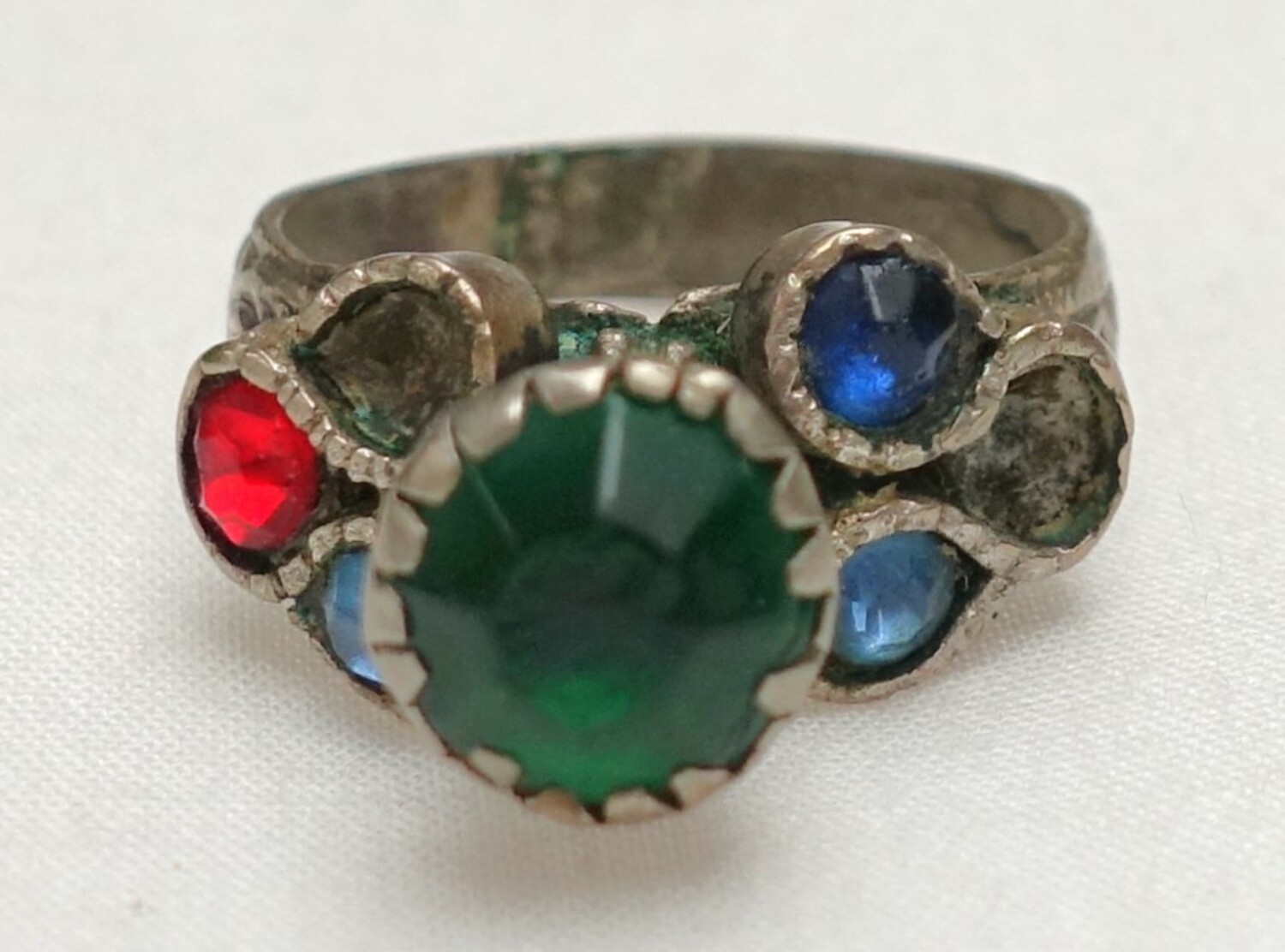 Silver ring with a decorated band with a cone holding a green glass circle, and flanked by three glass circles in red and blue. Afghanistan, 20th century (TRC 2024.1027).