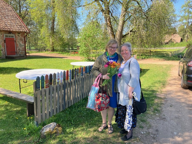 Merle Ernits and Gillian Vogelsang at the Heimtali Museum, Estonia; in the background a garden fence painted with knitted socks
