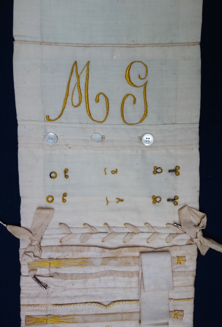 Detail of the corset sample with the initials M G, buttons, hooks and eyes, lacing, boning. (TRC 2023.2780).
